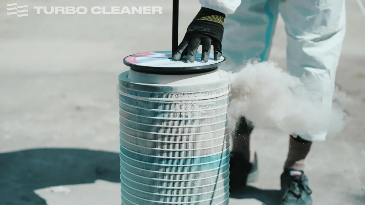 Operator blow-cleaning a cylindrical filter, dust exiting the element